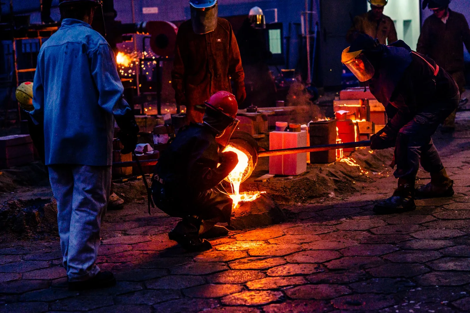 Foundry workers in protective gear pouring molten metal into moulds